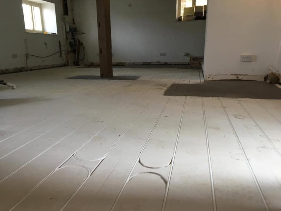 Underfloor heating pipe runs set into grooved floor panels across an open-plan room