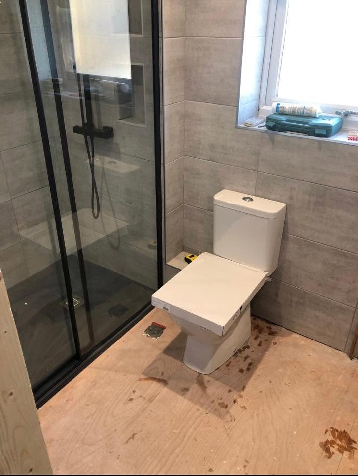 Bathroom installation in progress with a black-framed shower enclosure and new WC fitted