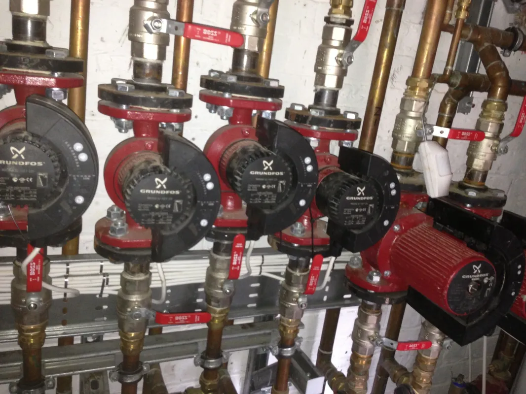 Four circulation pumps installed in line with red isolation valves on a heating system