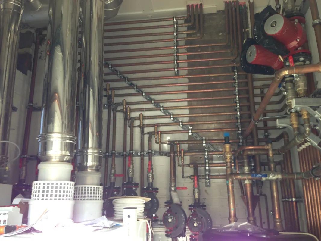 Bank of parallel copper heating pipes and circulation pumps in a finished plant room