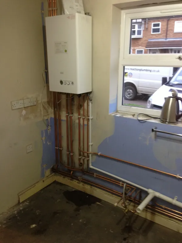 Boiler mounted on a freshly plastered wall with vertical copper flow and return pipes